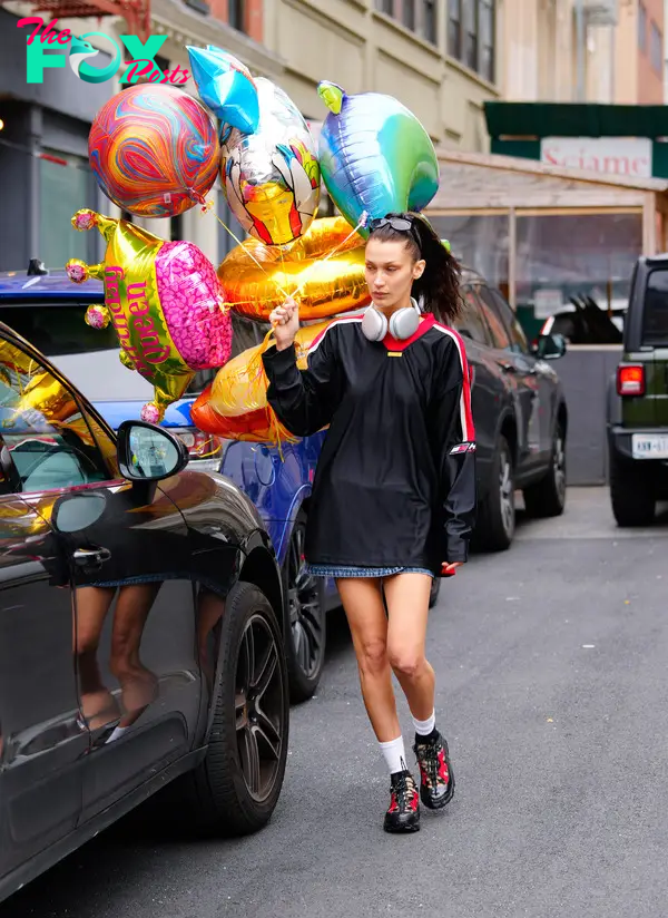 Bella Hadid carrying balloons and wearing headphones