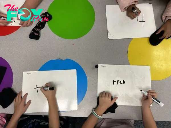 An overhead view of young kids writing on whiteboards