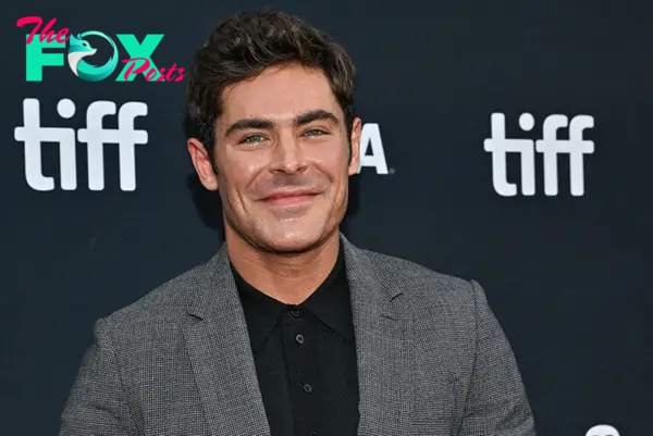 Closeup of actor Zac Efron smiling in a grey suit and black shirt at tiff.