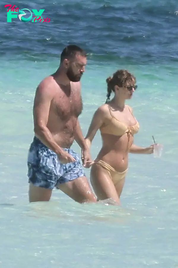 Taylor Swift and Travis Kelce walking on the beach together.