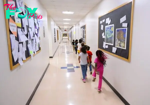 Young school kids walk in a single-file line through a school hallway