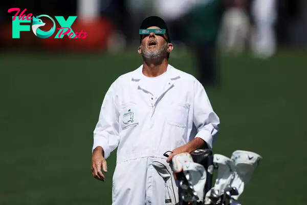 A caddie uses glasses to view the eclipse during a practice round prior to the 2024 Masters Tournament