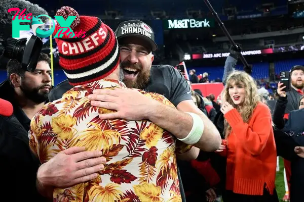 Jason and Travis Kelce hugging with Taylor Swift in the background. 
