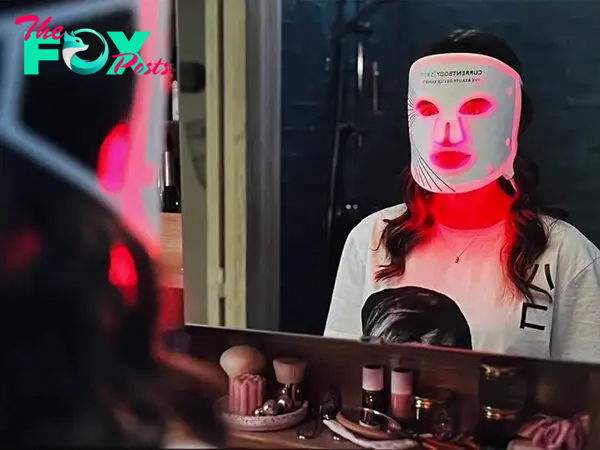 Lily Collins looking in a mirror while wearing the Current Body LED mask 