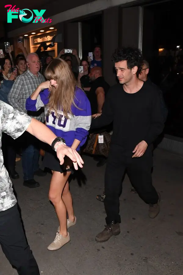 Taylor Swift and Matty Healy walking through a crowd at night