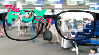 A pair of augmented reality glasses held up against an airport lounge backdrop.