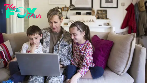 A military service person and two children sit together on a couch while using a laptop together