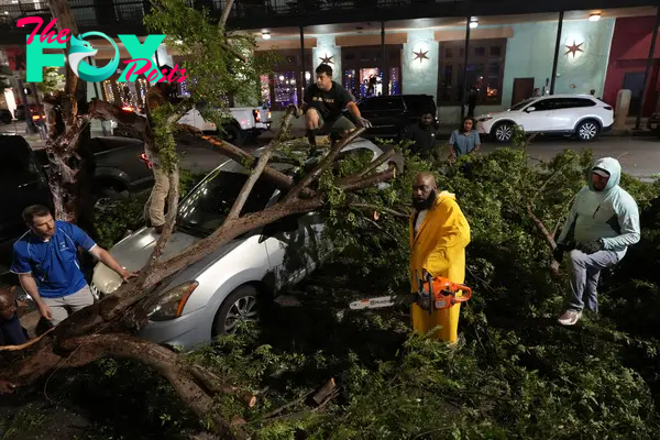 Rapper Trae tha Truth, in yellow, cuts fallen tree limbs on top of a car in the aftermath of a severe thunderstorm that passed through downtown, Thursday, May 16, 2024, in Houston.