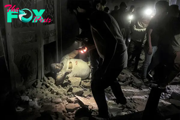 People approach with flashlights an injured person lying amidst rubble on the ground at the site of a building that was hit by Israeli bombardment in Rafah, southern Gaza Strip, on May 7, 2024 amid the ongoing conflict in the Palestinian territory..