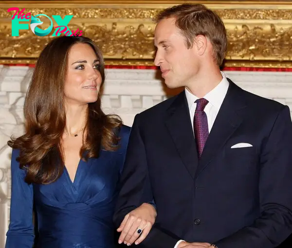 Kate Middleton with her arm through Prince William's as they stare into each other's eyes in front of a gold picture frame.