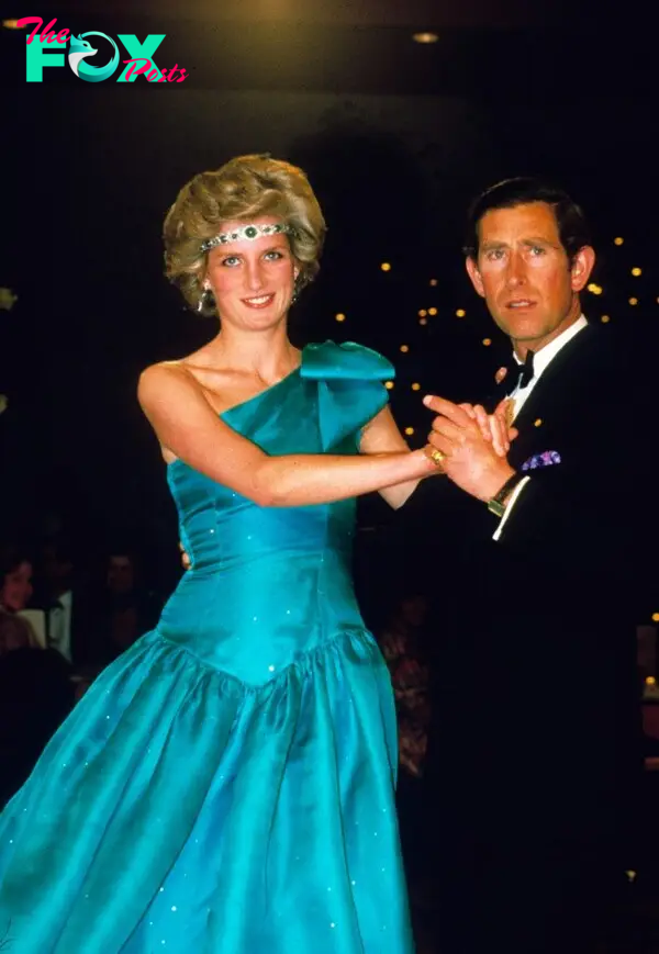 Princess Diana wearing a green emerald headband and aquamarine ballgown, holding hands with Prince Charles who is wearing a tuxedo.