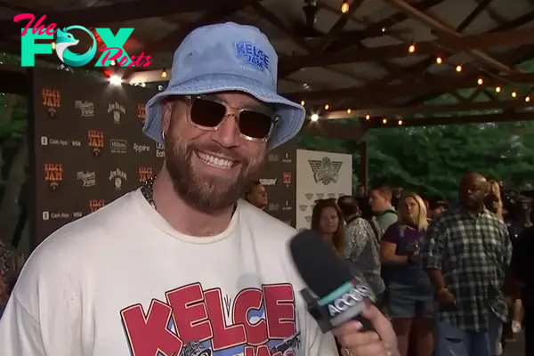 Travis Kelce wears a bucket hat and sunglasses in an interview.