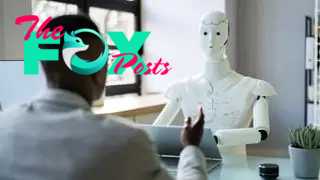 A robot sitting opposite a human who is gesturing with their hands.