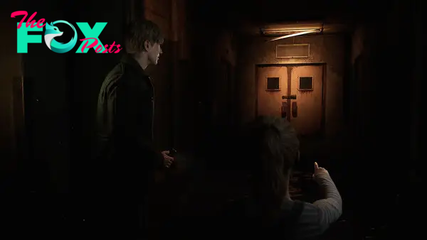 In this image, James stands to the left of the screen, staring at a rusted set of double doors at the end of a dark corridor. His gaze is directed that way by the pointed finger of a young girl who stands alongside him.