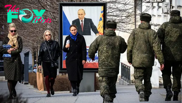 People walk in front of a poster showing Russian President Vladimir Putin and reading "The West doesn't need Russia. We need Russia!" in Simferopol, Crimea, on March 5, 2024.