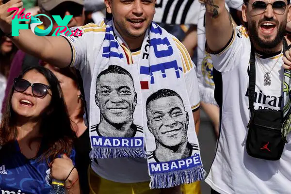 Supporters wearing football scarves depicting French footballer Kylian Mbappe cheer 