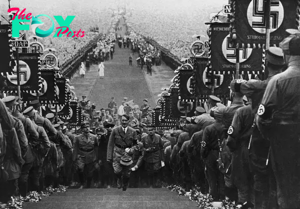 Adolf Hitler ascends the steps at Bückeberg, Germany, flanked by storm troopers holding banners displaying the the Nazi swastika, in 1934.