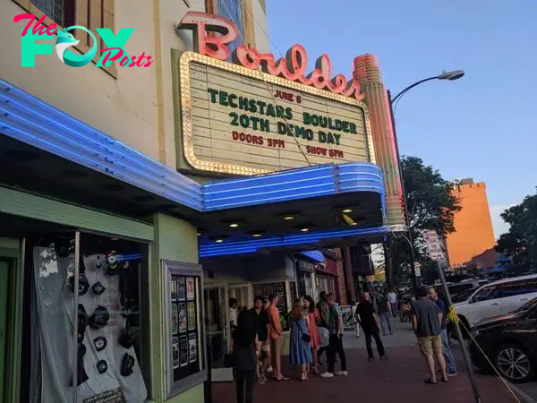 People gather outside a Boulder theater with a sign above that says "June 6 Techstars Boulder 20th Demo Day"