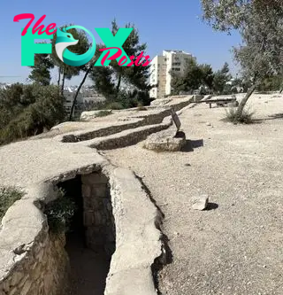 We see a stone trench by a dirt surface with a modern city in the background.