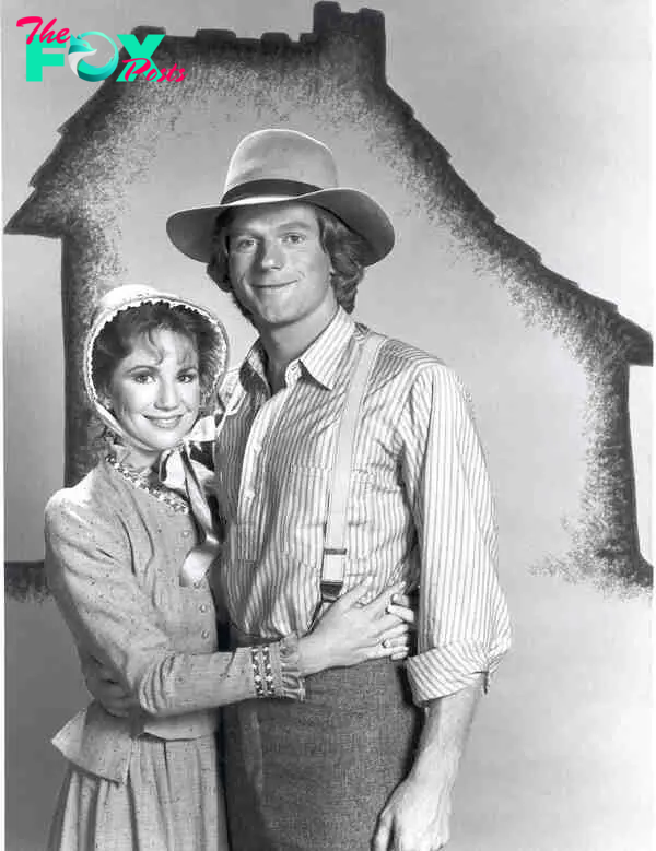 Melissa Gilbert and Dean Butler in period costumes, standing in front of a "Little House" outline. 