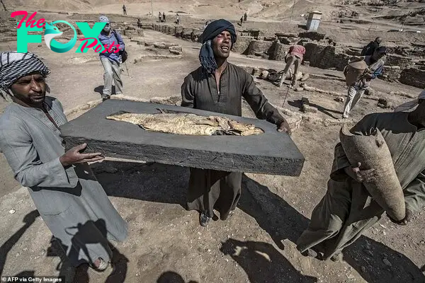 A picture taken on April 10, 2021, shows workers carrying a fossilised fish uncovered at the archaeological site