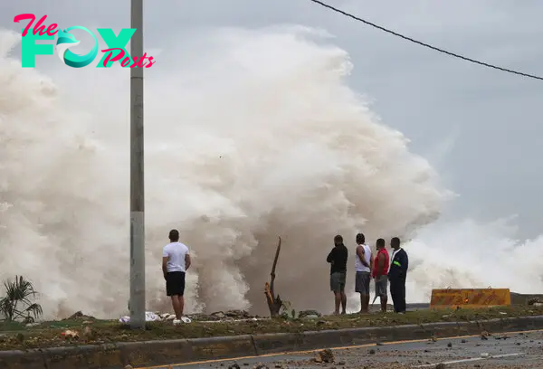 People stand in front of waves crashing against the shore as Hurricane Beryl moves south of the island, in Santo Domingo, Dominican Republic, on July 2, 2024.