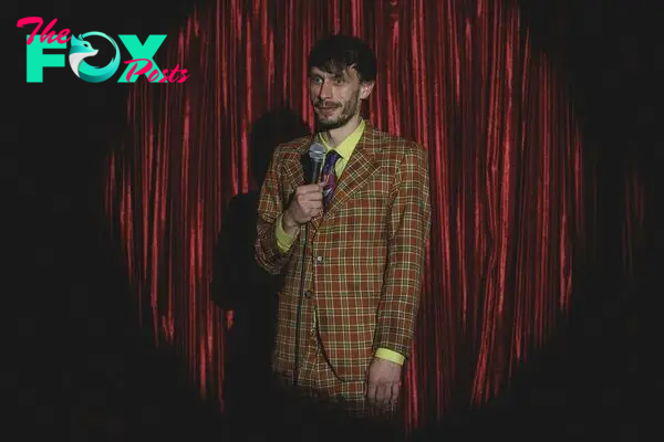 Richard Gadd in Baby Reindeer, standing in a loud suit with a microphone in a spotlight in front of a red curtain