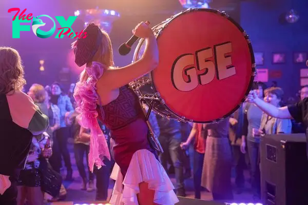 Summer (Busy Philipps) playing a drum with “G5E” printed on it