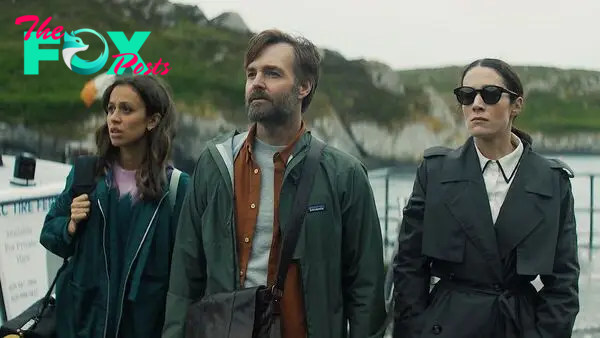 Will Forte, Siobhan Cullen, and Robyn Cara stand by the water with an Irish flag waving behind them in Bodkin
