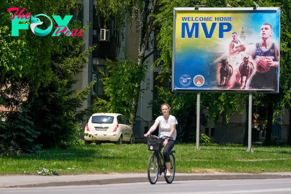 A woman rides a bicycle past a billboard showing Denver Nuggets center Nikola Jokic in his hometown of Sombor, Serbia, on June 18, 2023.