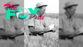 Black and white photo of American agronomist Norman Borlaug writing in a notebook whilst standing in a field of wheat.