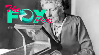 Black and white photo of American astronomer and suffragist, Annie Jump Cannon. She is sitting at a desk, carefully looking a spectroscope as she works on classifying stars.