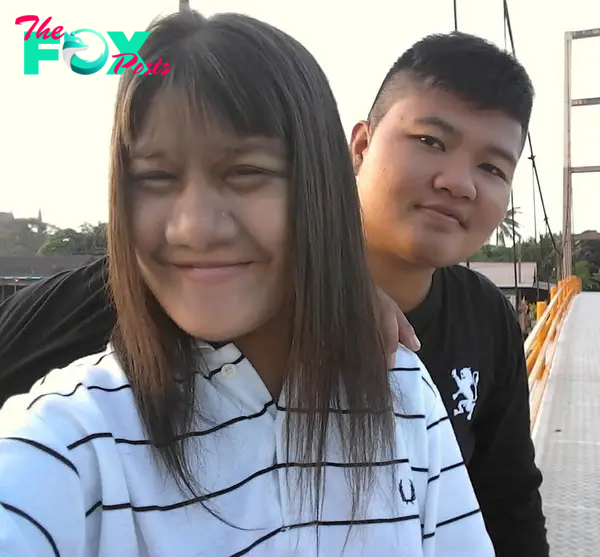 A young couple wearing hoodies posing for a photo on a bridge.