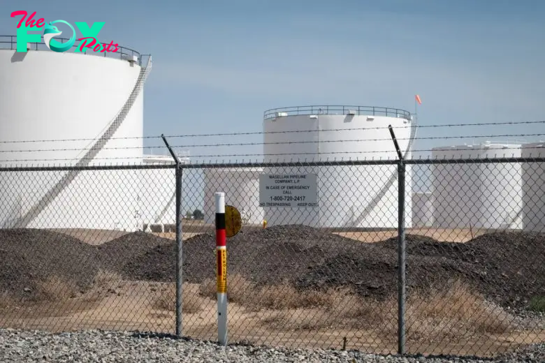 Large white storage tanks behind a chain-link fence at Magellan's Dupont gasoline storage facility, with a warning sign and emergency contact number visible.