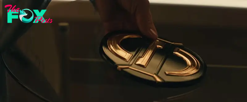 A shot of a hand picking up an round belt buckle, emblazoned with a gold ‘S’ (presumably for ‘Sentry’) in Thunderbolts*.