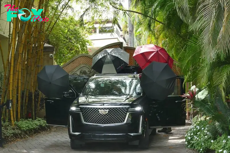 A man places umbrellas on a Cadillac Escalade outside Diddy's 2 Star Island Drive mansion in Miami Beach, Florida, on Wednesday, March 27, 2024. 