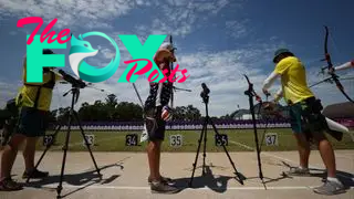 three archers stand with their backs to the camera preparing to shoot arrows toward targets in a field