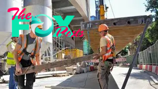 Construction workers lift steel truss on a building site.