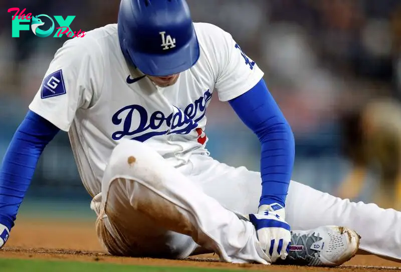 Freddie Freeman #5 of the Los Angeles Dodgers holds his right ankle after an injury running from home plate to first base on a ground out against first baseman Luis Arraez 