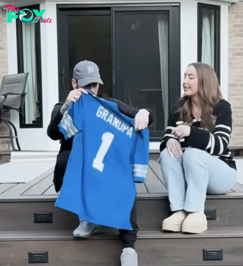 Eminem holds up a blue jersey that says &quot;GRANDPA&quot; with the number 1 next to smiling Hailie