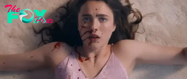 Close-up of a woman, played by Kathryn Newton, lying on the ground with blood splattered on her face, wearing a sleeveless top. Scene from a dramatic TV or movie moment