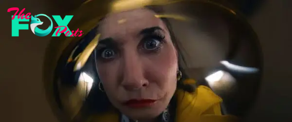 Close-up of a woman with wide eyes and a surprised expression, looking through a distorted lens. The woman is wearing a yellow garment