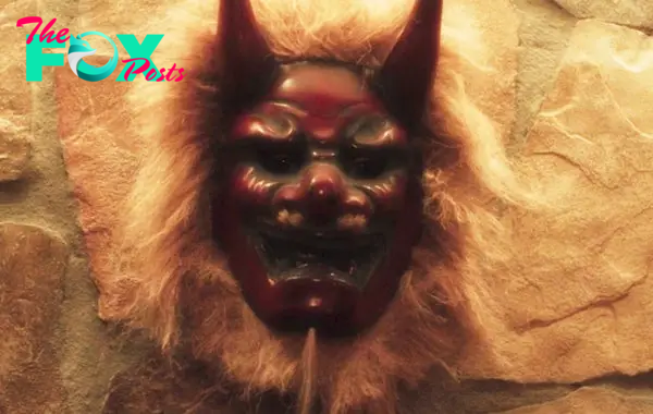 Decorative mask with horns and fur, resembling a demon or mythical creature, mounted on a stone wall