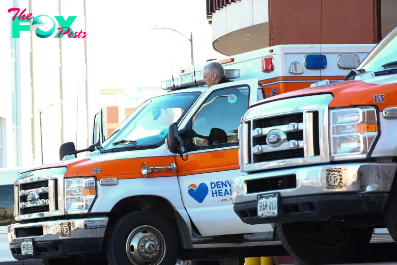 Two Denver Health ambulances parked outside a building, with a person visible in one driver's seat.