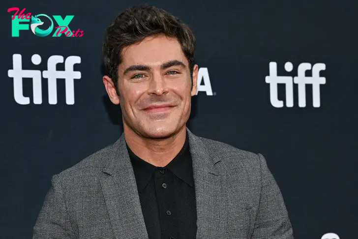 Closeup of actor Zac Efron smiling in a grey suit and black shirt at tiff.