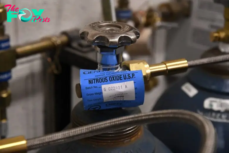 Close-up of a nitrous oxide cylinder with a blue label showing details like "Nitrous Oxide U.S.P." and a valve at the top.