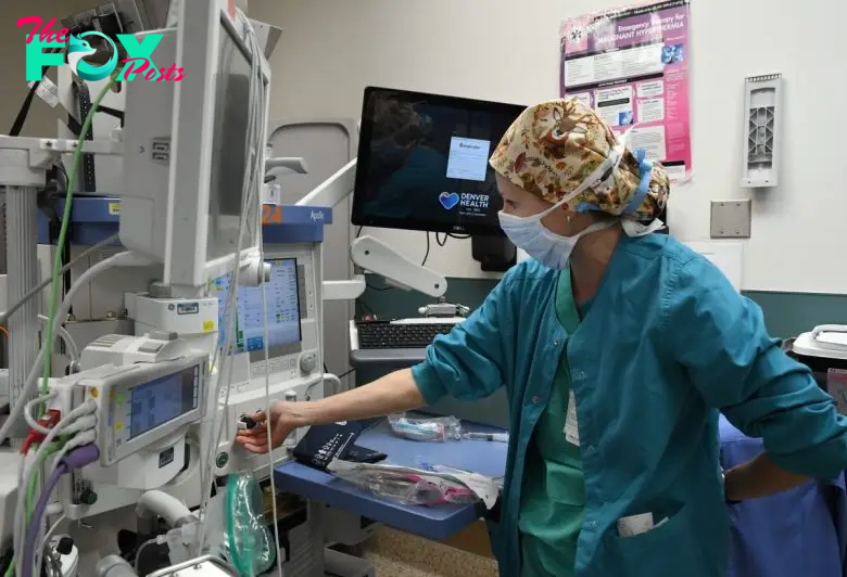 Medical professional in scrubs adjusts hospital equipment in a clinical setting.