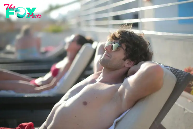 A happy man wearing sunglasses while lying on a sunbed | Source: Pexels