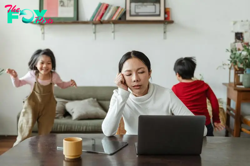 An exhausted woman sitting by a computer as her children play in the background | Source: Pexels