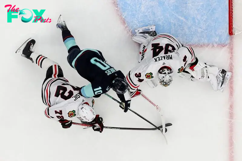 Matty Beniers #10 of the Seattle Kraken stickhandles against Alex Vlasic #72 and Petr Mrazek #34 of the Chicago Blackhawks